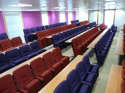 Lecture hall chairs in rows of contrasting purple and deep red with fixed writing desks