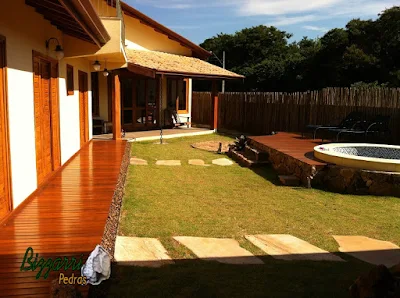 Caminhos de pedra no jardim com pedra São Tomé tipo pedra cacão com esse tipo de assentamento de pedra com junta de grama entre as pedras, caminho entre o deck de madeira no terraço da casa até a piscina com execução do deck de madeira na piscina e execução do paisagismo em casa em condomínio em Atibaia-SP.