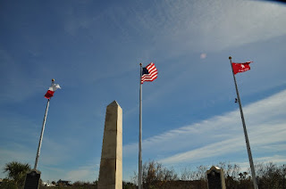 U.S. flag with a Texas flag and a Jane Long flag as well as an obelisk and two historical markers.