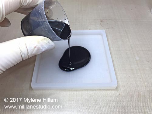 Pouring black resin into the base of the square silicone coaster mould.