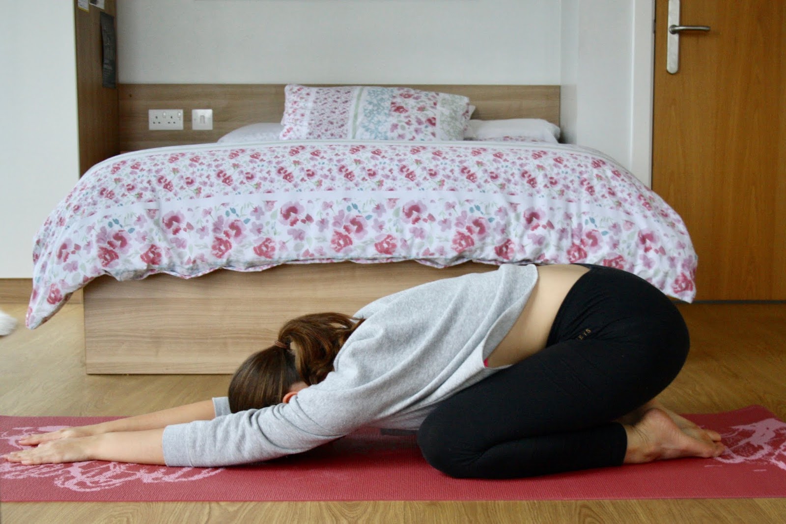 abbey is demonstrating child's yoga pose, kneeling on the floor and stretching her hands out in front of her