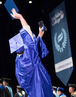 Image of dual enrollment student in cap and gown taking a selfie at graduation