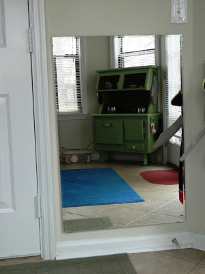 Photo of Montessori-friendly playroom with blue rug, wood table and chairs,  wood bookcase, dress-up clothes, and a wall mirror