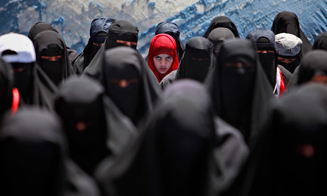 Kvinde med rødt tørklæde kigger op under bøn ved protest demonstration mod Yemens præsident