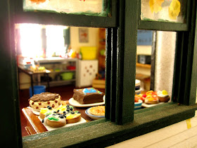 View from a miniature dolls' house veranda to inside where there is a table laden with cakes.