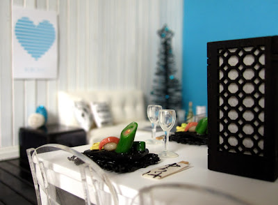 Modern one-twelfth scale miniature scene in white and teal, showing two sushi meals on a table and a Christmas tree in the background.