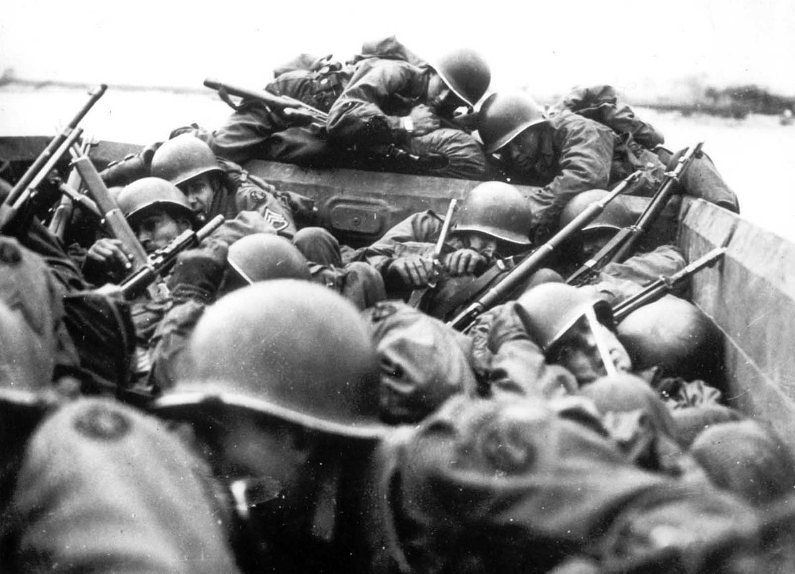 American soldiers aboard an assault boat huddle together as they cross the Rhine river at St. Goar, Germany, while under heavy fire from the German forces, in March of 1945. 