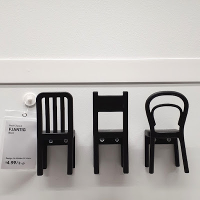 Three IKEA chair-shaped hooks hanging on a wall with a price tag next to them.