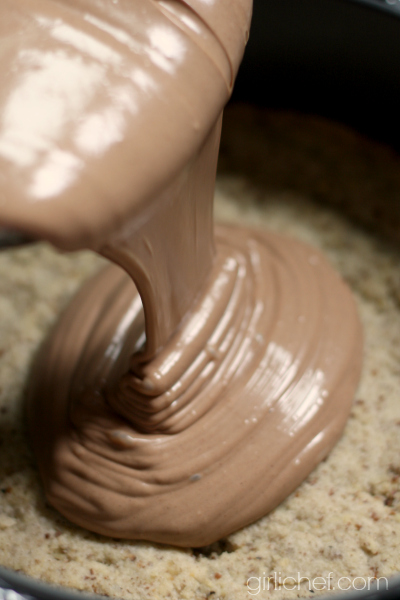 chocolate cheesecake filling being poured onto a par-baked pecan shortbread crust