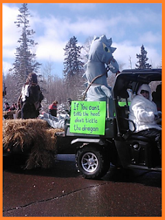 "If you can't take the heat, don't tickle the dragon" on a green sign that hangs beside a gray dragon.