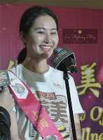 A female participant of the Miss Chinese World from Shang Hai smilling happily in front of a microphone