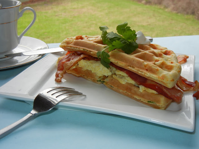 bacon and egg waffle sandwich on a plate with tea in the background and a fork to the left 