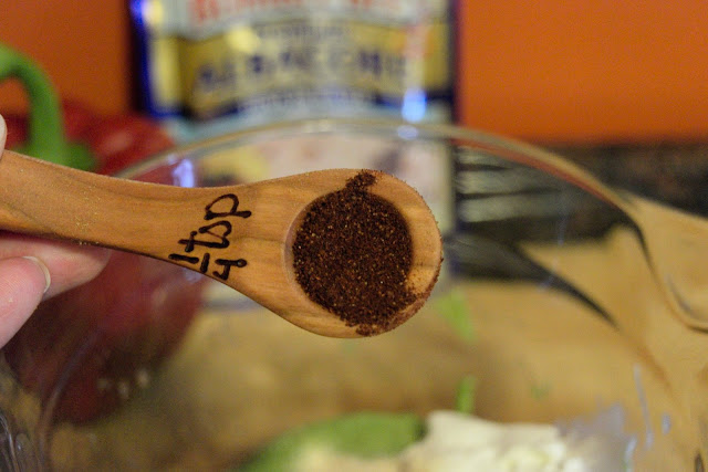 A picture of a measuring spoon, over a mixing bowl, with chili powder in it.