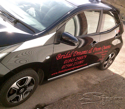 Photograph of the side of the car for the wedding shop, Bridal Dreams and Prom Queens vehicle livery. Featuring red vinyl text on a black Toyota car.