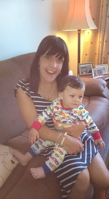 picture of amelia in a striped dress holding a one year old elliot on her lap, elliot is wearing a babygro, amelia is smiling at the camera