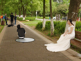 young woman wearing a wedding gown sitting on a bench at a park