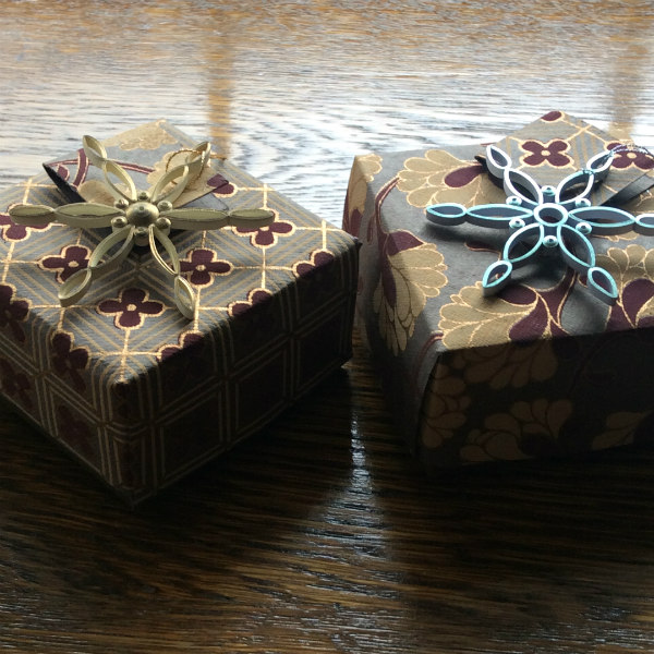 Two hand folded paper boxes topped with modern quilled snowflake ornaments
