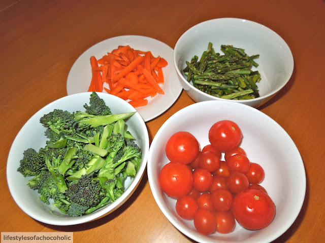 raw carrots, broccoli, asparagus and tomatoes all in separate white bowls 