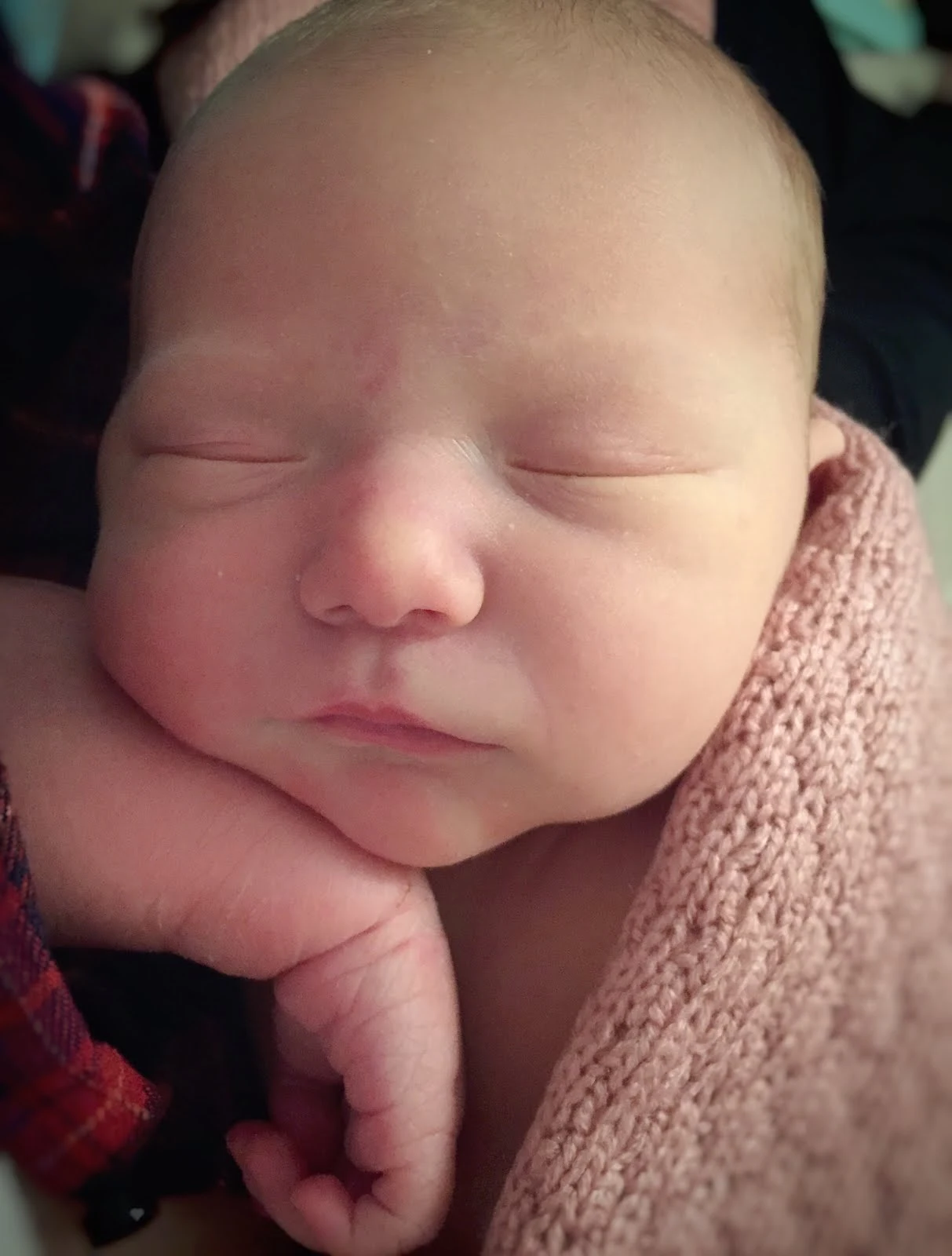 A close up of a newborn baby with her eyes closed resting on her arm