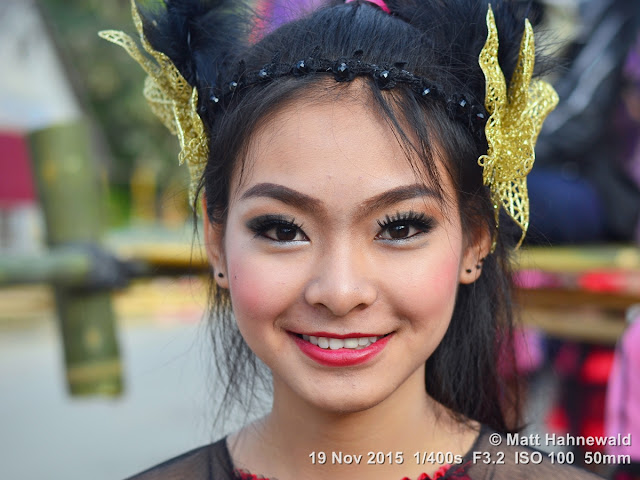 Matt Hahnewald; Facing the World; Asia; Northern Thailand; Mae Chaem; people; closeup; portrait; street portrait; headshot; smiling; Thai girl; Thai smile; Land of Smiles; world cultures; travel; eye contact; Nikon DSLR D3100; 50 mm prime lens; colour; face; outdoor; street parade; make-up; beautiful; folk costume; Lanna tradition; dressed up to the nines; lip make-up