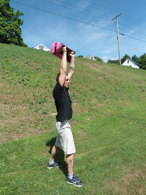 Man holding the Ultimate Sandbag overhead outdoors on a grassy field
