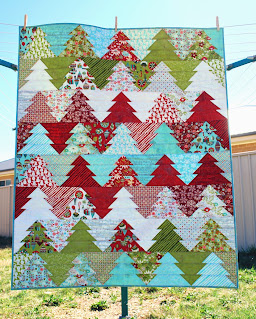 A tree quilt in christmas fabrics of red, green, white and aqua. It features trees arranged so that they form a zigzag pattern across the quilt.