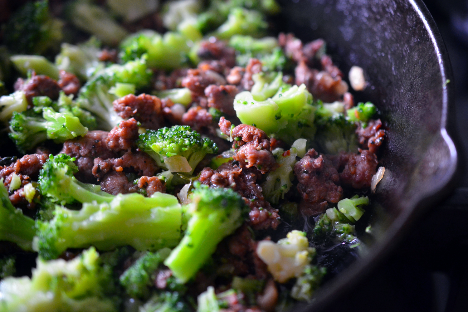 A close up of a cast iron frying pan filled with leftover ground meat and cut up frozen broccoli.