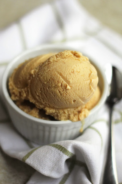 Two scoops of cookie butter ice cream contained in a round, white bowl next to a spoon