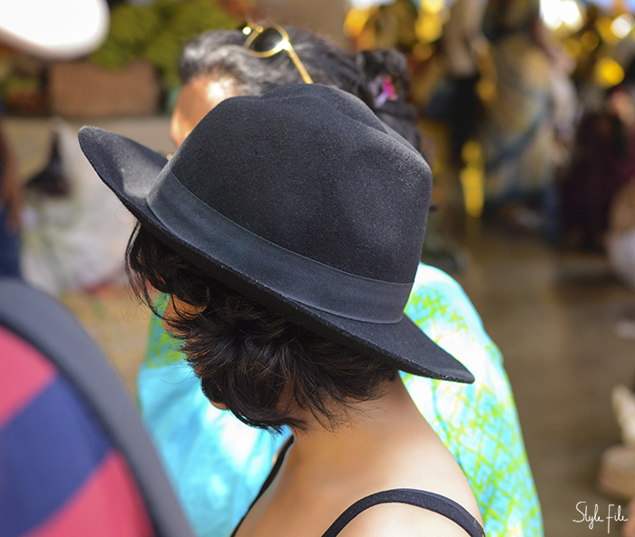 Image of a woman wearing a black flat rimmed hat over short hair with a strap blouse