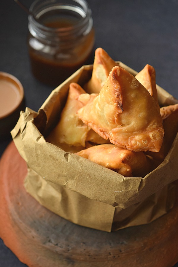 A top look of a brown  paper bag having crisp fried Onion Samosa served with chai and date chutney