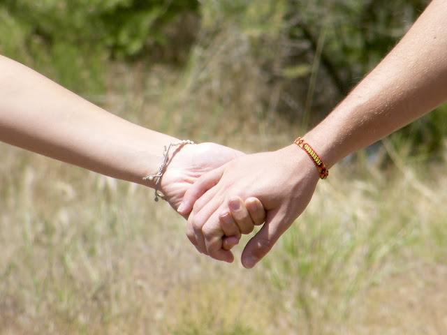 Young lovers hold hands in a field of grasses.