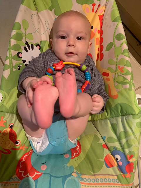 Baby Boy in a Fisher Price bouncer holding on to his feet