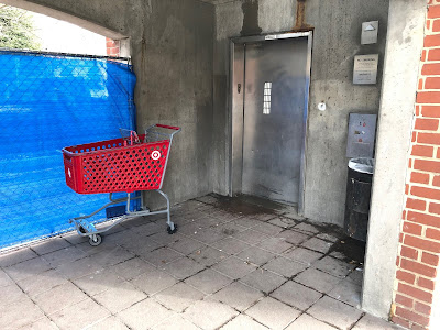 Photo of an elevator. There is a Target cart in front of it, some wet tiles, and detritus on the ground.