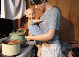 Full-scale model of a 1930s woman cooking dinner, while holding a baby and having her apron tugged by a screaming child.