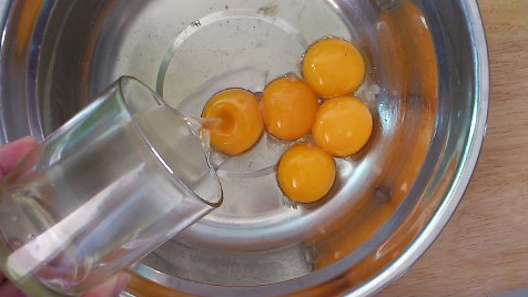 adding coconut oil to egg yolks in a mixing bowl