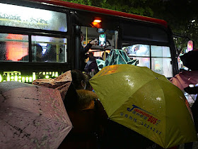 Person boarding a bus with a yellow Jumbo Wuzhou Bus umbrella.
