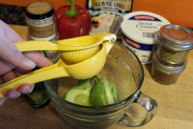 A picture of a lemon being juiced over the avocado in the mixing bowl.  