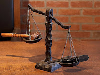 A balance scale, with a gavel on one side, and a pistol on the other. The pistol is lower due to being heavier.
