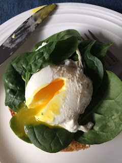 paoched egg with broken yolk over spinach and a english muffin 
