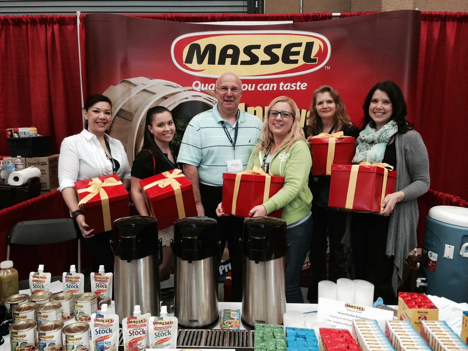 bloggers at the Gluten-Free & Allergy-Friendly Expo holding boxes of Massel products behind a table of Massel products