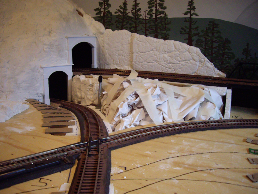 Cardboard strips and crumpled paper balls being applied to model railroad benchwork to form hard shell terrain
