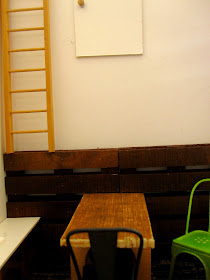 Modern dolls' house miniature half-built cafe, showing a wall with a cupboard near the ceiling and a ladder leading to it.