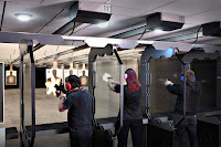 Bir poligonda tabanca ve tüfeklerle önlerindeki hedeflere atış yapan bayan ve erkekler