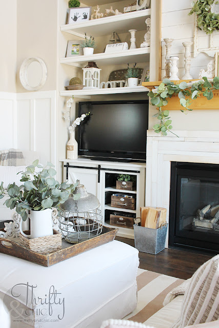 living room with white couch, large window, stacked wood, and shiplap mantel