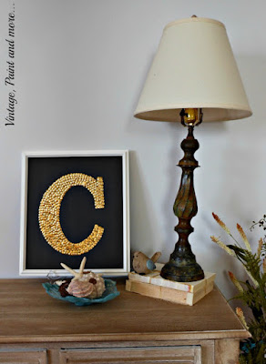 DIY monogram art done with thumbtacks and chalkboard painted core board displayed with seashells and vintage lamp