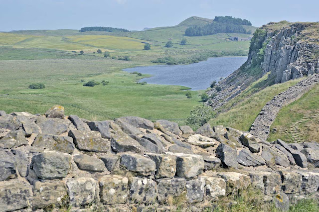 A section of the Wall in the foreground, with crags and a lake beyond