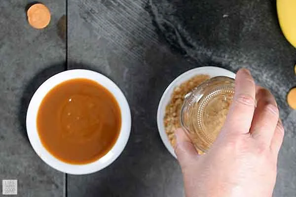 Dipping serving glass into caramel and then crushed cookies for banana pudding milkshake