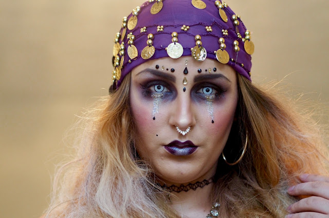 fortune teller makeup look with purple headscarf and coins, gold earrings and gems on the face. 