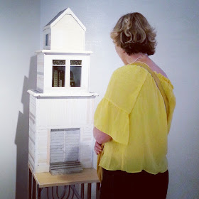 Woman standing in front of a miniature building in an art gallery.