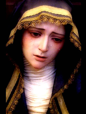 La Virgen con una toca negra y bordes dorados. Está llorando.